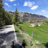 Strada di montagna, un'avventura in moto verso la punta veleno. Paesaggio verdeggiante, montagne innevate e cielo azzurro.