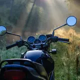 Manubrio di moto scura in un prato nebbioso, pronto per esplorare i borghi lombardia in moto all'alba.