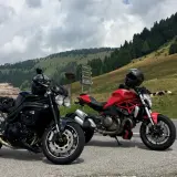 Due moto, una nera e una rossa, parcheggiate sul ciglio della strada al passo Castrin. Mucche al pascolo sullo sfondo di un prato verde e alberi.