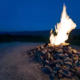 Fuoco acceso su un cumulo di pietre, con le colline del monte Busca sullo sfondo al crepuscolo.