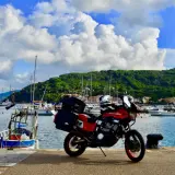 Moto pronta per l'avventura: Isola d'Elba in moto 3 giorni. Porto con barche e collina verde sullo sfondo.