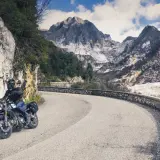 Motociclista su strada panoramica toscana, con montagne di marmo sullo sfondo.