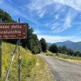 Cartello stradale indica Passo della Scalucchia a 1367 metri. La strada sale tra alberi e montagne sullo sfondo.