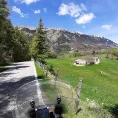 Strada di montagna, un'avventura in moto verso la punta veleno. Paesaggio verdeggiante, montagne innevate e cielo azzurro.