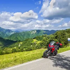 Ducati rossa ferma sul ciglio della strada statale 67, con un panorama mozzafiato di colline verdi e cielo azzurro.