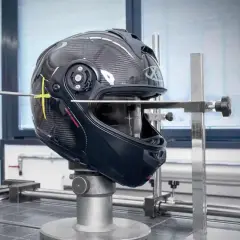 Casco da moto in carbonio sottoposto a test per l'omologazione, con strumenti di misurazione che ne verificano la resistenza e la sicurezza.