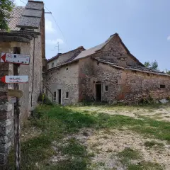Un vecchio parparo in pietra, con tetto in lamiera e tegole, mostra cartelli per sentieri escursionistici e ciclabili.