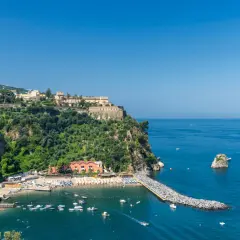 Vico Equense cosa vedere: una baia con spiaggia attrezzata, un molo di rocce e un borgo arroccato sulla scogliera.