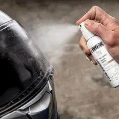 Mano spruzza prodotto su visiera casco per renderla priva di graffi e migliorare la visibilità in caso di pioggia.