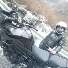 Panoramica Zegna moto con motociclista in giacca di pelle, accanto a una cascata.