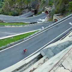 Ciclista solitario affronta i tornanti del passo Bidibidì, tra gallerie scavate nella roccia e panorami mozzafiato.