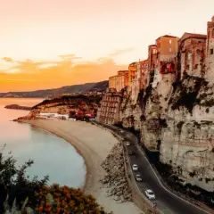 Tramonto mozzafiato sulla costa, con case aggrappate alla scogliera. Un sogno di **Calabria in moto**.