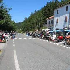 Gruppo di motociclisti in sosta lungo la strada statale 67 Tosco Romagnola, con moto parcheggiate e un hotel sullo sfondo.