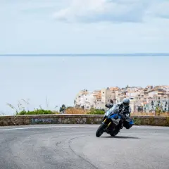 Motociclista in curva su strada panoramica, con il mare e il borgo di Sperlonga sullo sfondo. Un viaggio da Terracina a Sperlonga.