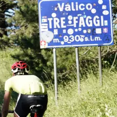 Ciclista in cima al valico Tre Faggi, 930 metri sul livello del mare, tra alberi e erba alta.