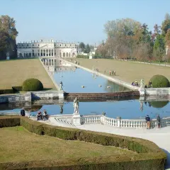 Un'imponente villa con un lungo specchio d'acqua e giardini curati, che ricorda le ville palladiane.