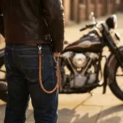 Un uomo in giacca di pelle e jeans, con una catena intrecciata al portafoglio, accanto a una moto. Ecco chi sono i bikers: liberi e con stile.