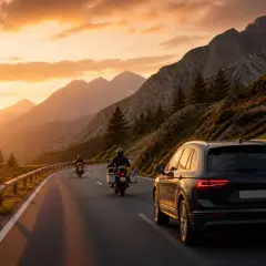 Due moto e un'auto percorrono la SS 439 al tramonto, tra montagne maestose e un cielo infuocato.