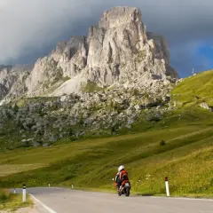 Motociclista in viaggio verso il passo del cerro, con imponenti montagne sullo sfondo e verdi pendii erbosi.