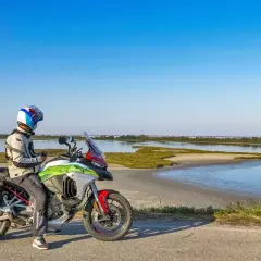 Motociclista con moto da turismo si ferma lungo la strada statale 9 Via Emilia, con una laguna sullo sfondo.