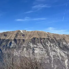 Vetta del monte Pizzoc con neve residua, pendii bruni e rocce bianche sotto un cielo azzurro con scie di aerei.