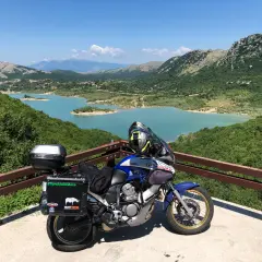 Moto pronta per esplorare gli Appennini, con un lago turchese e montagne verdi sullo sfondo. #AppenniniInMoto