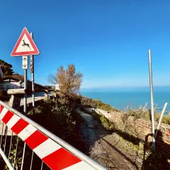 Panoramica Gabicce con segnale di pericolo cervi e mare azzurro. Strada sterrata con muretto in mattoni.
