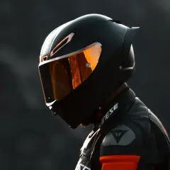 Un motociclista indossa un casco integrale nero con visiera arancione riflettente, pronto per la pista.