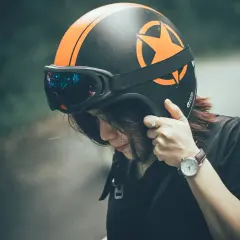Ragazza con casco da moto nero e arancione, occhiali riflettenti. Dove mettere il casco della moto? Forse qui, prima di partire.
