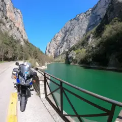 Moto parcheggiata lungo la strada panoramica delle Gole del Furlo, con il fiume color smeraldo e le imponenti pareti rocciose.