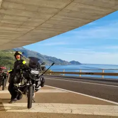 Motociclisti in sosta panoramica, con moto pronte per esplorare la costa tra Alghero e Oristano. Mare azzurro e montagne sullo sfondo.