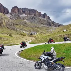 Motociclisti in gruppo affrontano le curve del passo della Cappelletta, tra verdi pendii e imponenti pareti rocciose.