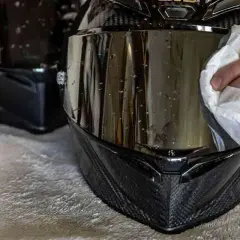 Mano che pulisce la visiera del casco con un panno bianco, rimuovendo insetti e sporco per una guida sicura.