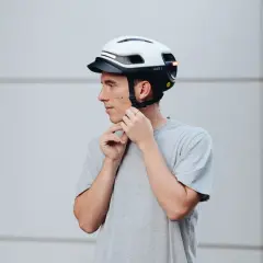Uomo con casco bianco e nero, che regola gli spallacci. Le taglie caschi sono fondamentali per la sicurezza.