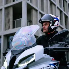 Motociclista con casco modulare, che può essere jet o integrale, pronto a partire con la sua moto davanti a un edificio moderno.