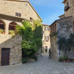 Un vicolo pittoresco a Montemerano, con case in pietra, archi, piante rampicanti e un cielo azzurro. Scopri cosa vedere in questo borgo incantevole.
