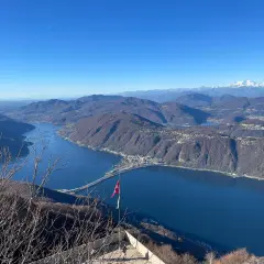 Vista mozzafiato dal balcone d'Italia. Un lago blu intenso abbraccia montagne boscose, con un ponte che attraversa le acque. Perfetto per un viaggio in moto.