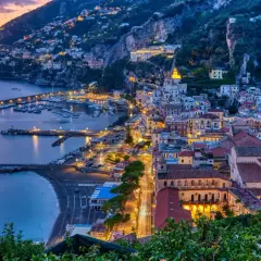 Le luci illuminano le case aggrappate alla costa e il porto turistico. Le strade costiera amalfitana prendono vita al tramonto.