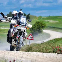 Coppia in moto su sterrato, seguendo una mappa percorso eroica in moto tra colline verdi.
