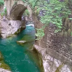 Acqua smeraldo scorre sotto un antico ponte di pietra, creando un'atmosfera suggestiva nell'orrido Val Taleggio.