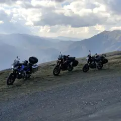 Tre moto attendono al Passo dell'Abetone, con un panorama montano mozzafiato sotto un cielo nuvoloso.
