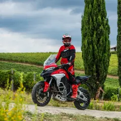 Un motociclista in tuta rossa sfreccia tra i cipressi e i vigneti del Val d'Orcia in moto.