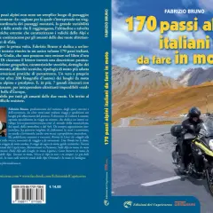 Motociclista in cima a un passo alpino, con montagne sullo sfondo. Un invito a scoprire 170 passi alpini italiani da fare in moto.