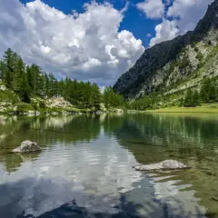 Un lago alpino tranquillo riflette il cielo nuvoloso e le montagne boscose. Un paesaggio mozzafiato dei laghi della Valle d'Aosta.