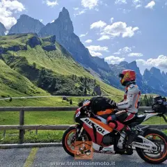 Motociclista in tenuta da gara su una Honda Repsol, con lo sfondo delle maestose vette del Passo Cereda.