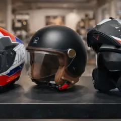 Tre caschi da moto: uno bianco con grafiche rosse e blu, uno nero vintage con dettagli in pelle, e uno bianco e nero sportivo. Snell e1.