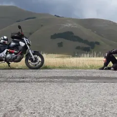 Motociclista in tenuta da gara seduto sul ciglio della strada al passo San Antonio, con la sua moto parcheggiata accanto.