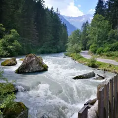 Fiume impetuoso tra rocce e boschi, con una strada serpeggiante e montagne sullo sfondo, ricorda le cascate del Nardis.