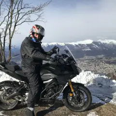 Motociclista con casco stellato su un balcone d'Italia innevato, con vista su montagne e città.