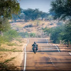 Un motociclista solitario affronta una strada tortuosa, immerso in un paesaggio arido e verdeggiante. Le sue gite in moto lo portano verso l'orizzonte.
